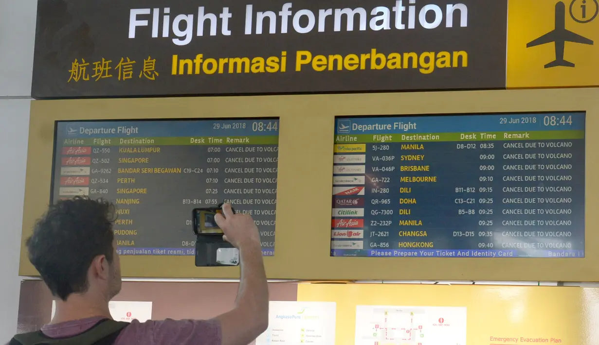 Calon penumpang mengambil gambar papan informasi penundaan penerbangan di Bandara Ngurah Rai, Bali, Jumat (29/6). Pihak pengelola menutup sementara aktivitas bandara maupun penerbangan karena gangguan abu vulkanis erupsi Gunung Agung. (AFP/GEDE ARDIASA)