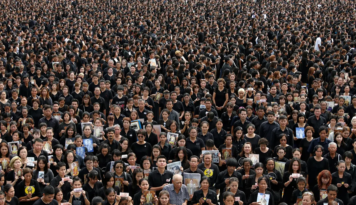 Puluhan ribu pelayat berpakaian hitam berkumpul di luar Grand Palace sambil menyanyikan rekaman lagu kerajaan, di Bangkok, Thailand, (22/10). Sebagian mereka membawa foto dan poster untuk menghormati raja mereka. (REUTERS/Jorge Silva)