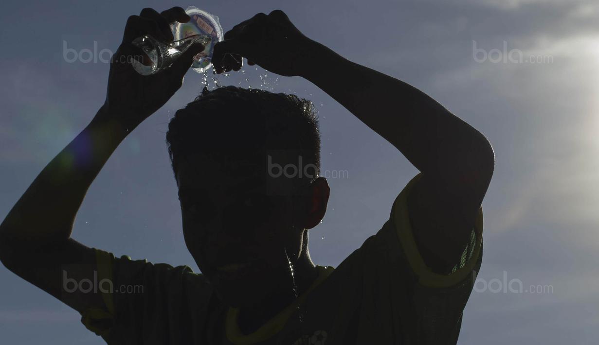 Seorang anak menghindari dehidrasi dengan membasahi kepalanya saat mengikuti turnamen Liga Remaja UC News di Lapangan Masariku Yonif 733, Ambon, Rabu (29/11/2017). (Bola.com/Peksi Cahyo)