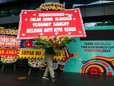 Seorang petugas membawa karangan bunga di kantor PSSI yang terletak di GBK Arena, Senayan, Jakarta, Kamis (30/03/2023) sebagai respon pembatalan Indonesia sebagai tuan rumah Piala Dunia U-20 2023 oleh FIFA. (Bola.com/Bagaskara Lazuardi)