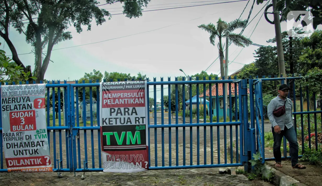 Warga melintas di samping spanduk meminta pelantikan RT di Meruya di Perumahan Taman Villa Meruya (TMV) Meruya Selatan, Kembangan, Jakarta Barat, Sabtu (26/2/2022). (Liputan6.com/Faizal Fanani)