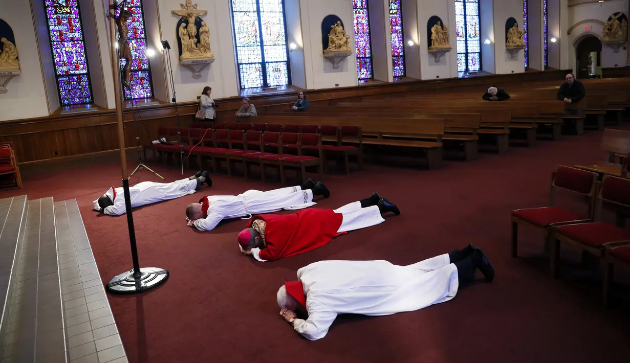 Uskup William Joensen (tengah) dan Pastor John Bertogli (kanan) berbaring di depan salib dengan sesama anggota klerus saat kebaktian Jumat Agung selama pandemi virus corona COVID-19 di Katedral St. Ambrose, Des Moines, Lowa, Amerika Serikat, Jumat (10/4/2020). (AP Photo/Charlie Neibergall)