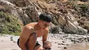 Pelan-pelan, suami Nikita Willy, mengenalkan air kepada anaknya. Sang bayi yang mengenakan kacamata hitam ini didudukan di pasir. (Foto: Instagram/@indpriw)