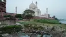 Pemandangan Taj Mahal dari seberang parit di tepi sungai Yamuna, Agra, India, Jumat (4/5). Kini, warna Taj Mahal  yang seharusnya putih marmer berubah menjadi kuning bahkan cokelat dan hijau di sejumlah sisinya. (AFP/CHANDAN KHANNA)