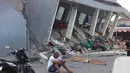 Seorang pria memeriksa ponselnya di dekat bangunan yang runtuh akibat gempa bumi di Reok, Provinsi Nusa Tenggara Timur, Indonesia, Minggu, 16 Agustus 2026. (Foto AP/Aquila Handayani Abbas)