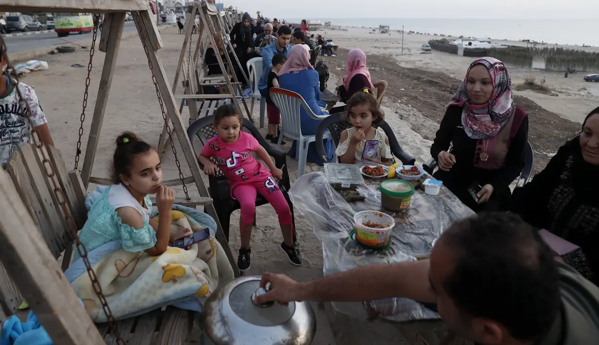 Anggota keluarga menyiapkan makanan mereka sambil menunggu berbuka puasa saat bulan suci Ramadan di pantai Kota Gaza, Palestina, Kamis (21/5/2020). Di tengah pandemi COVID-19, berbuka puasa bersama di pantai Kota Gaza tetap ramai. (AP Photo/Adel Hana)