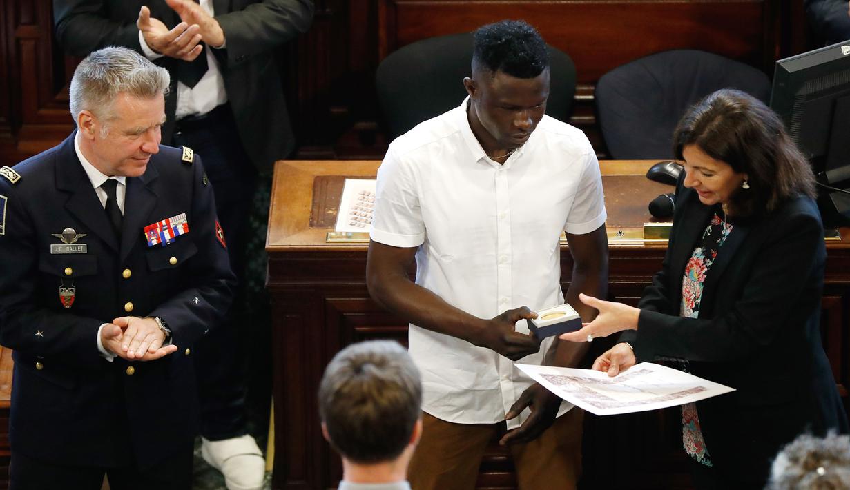 Imigran Mali Mamoudou Gassama menerima medali Grand Vermeil yang diberikan walikota Paris Anne Hidalgo (kanan) di Paris, Prancis (4/6). Mamoudou Gassama merupakan imigran gelap dari Mali yang tinggal di Prancis. (AFP/Francois Guillot)