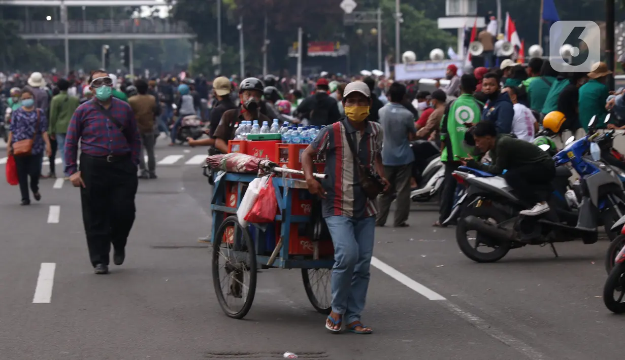 Pedangang menawarkan dagangannya kepada massa aksi saat demo penolakan omnibus law di kawasan patung kuda, Jakarta, Selasa (20/10/2020). Para pedagang kaki lima memanfaatkan moment aksi massa untuk mencari ke untungan meskupun sangat membahayakan bagi keselamatan mereka. (Liputan6.com/Angga Yuniar)