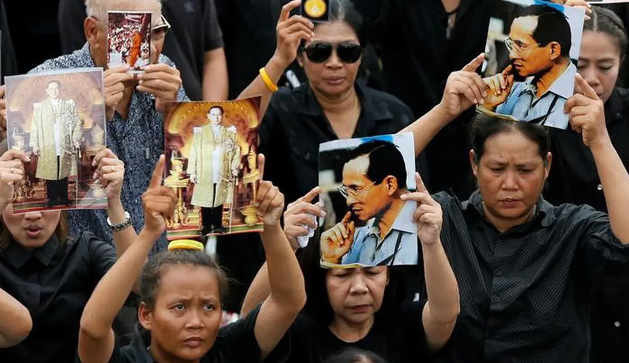 Sejumlah pelayat memegang foto Raja Bhumibol Adulyadej saat berkumpul di luar Grand Palace sambil menyanyikan rekaman lagu kerajaan, di Bangkok, Thailand, (22/10). Raja Bhumibol meninggal pada 13 Oktober di usia 88. (REUTERS/Jorge Silva)