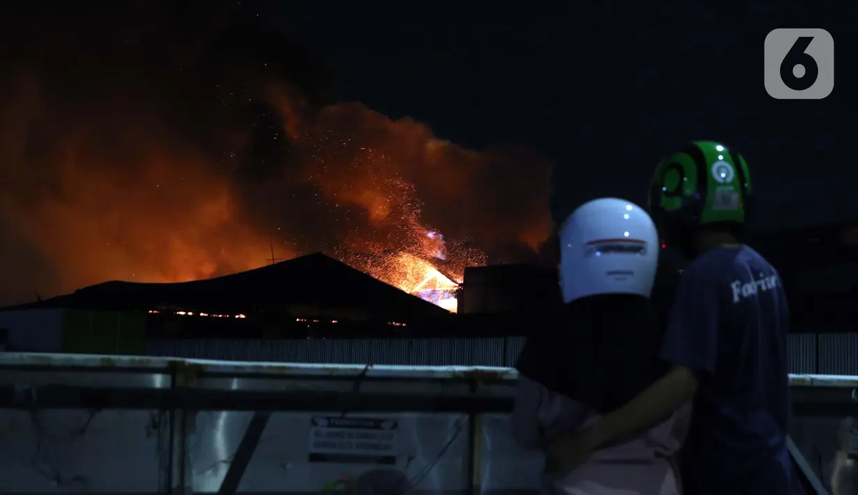 Warga melihat api yang membakar atap bioskop Grand di kawasan Senen, Jakarta, Kamis (8/10/2020). Unjuk rasa menentang disahkannya Omnibus Law UU Cipta Kerja berujung aksi anarkis merusak berbagai fasilitas umum. (Liputan6.com/Helmi Fithriansyah)