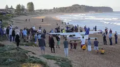 Orang-orang berdiri di dekat sebuah pesawat ringan yang mendarat darurat di sebuah pantai di Sydney, Rabu (26/5/2021). Pesawat kategori rekreasi itu mendarat selamat di pantai Sydney dengan tiga orang di dalamnya termasuk seorang bayi setelah mengalami kerusakan mesin. (AP Photo/Mark Baker)