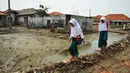 Dua orang siswi melewati pelataran bekas rumah yang terkena dampak abrasi di pantai Muara Gembong, Bekasi, Selasa, (26/7). Tingkat abrasi yang tinggi menyebabkan sejumlah rumah terkikis dan beberapa sekolah terendam air laut. (Liputan6.com/Gempur M Surya)