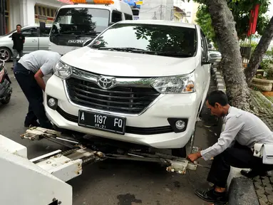 Petugas Dishub DKI memasang alat derek pada mobil yang parkir liar di kawasan Pasar Baru, Jakarta, Senin (27/6). Penertiban rutin ini dilakukan untuk membuat efek jera bagi warga yang masih parkir sembarangan. (Liputan6.com/Gempur M Surya)