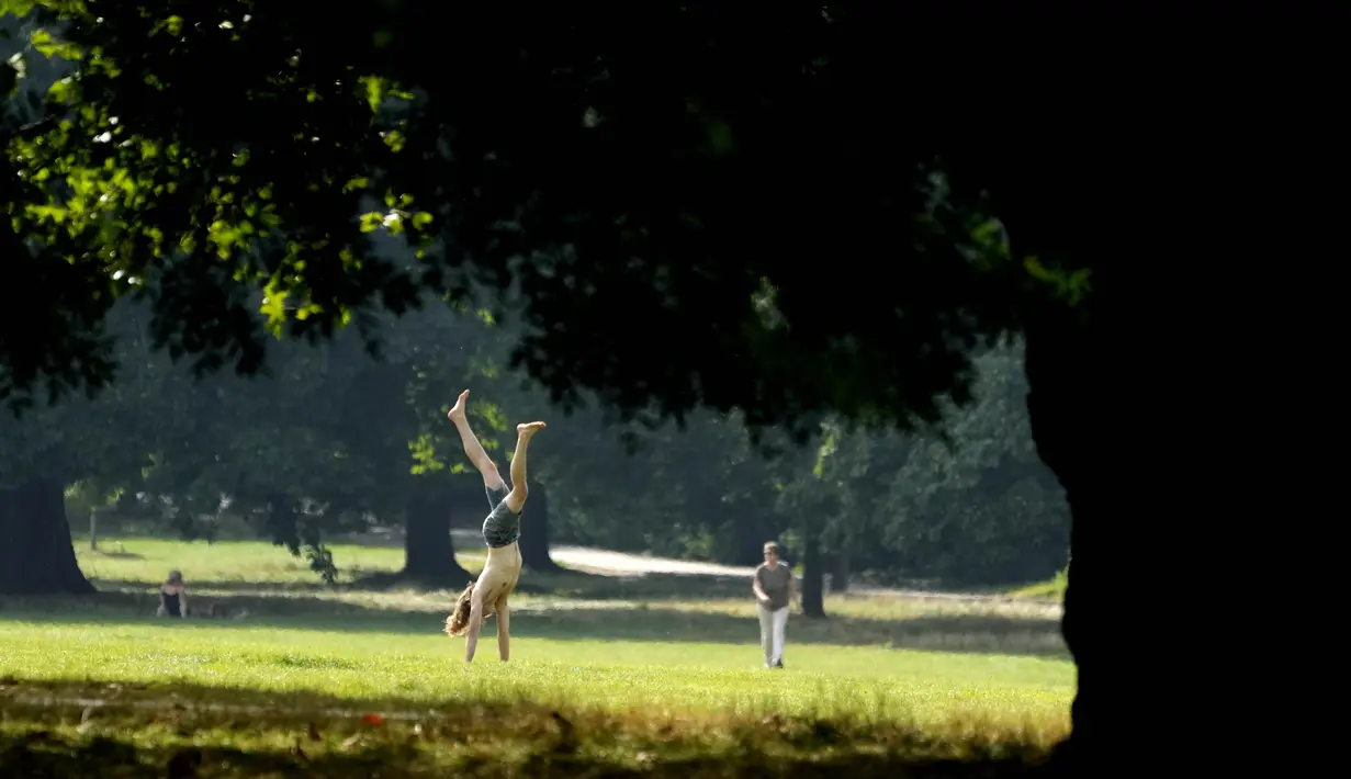 Seorang pria berlatih handstand di sebuah taman di London, Senin (6/7/2021).  Musim panas di Inggris kembali, dengan suhu di atas dua puluhan dan banyak sinar matahari. Peramal cuaca memperkirakan hingga 30 derajat Celcius di Inggris tengah. (AP Photo0/Frank Augstein)