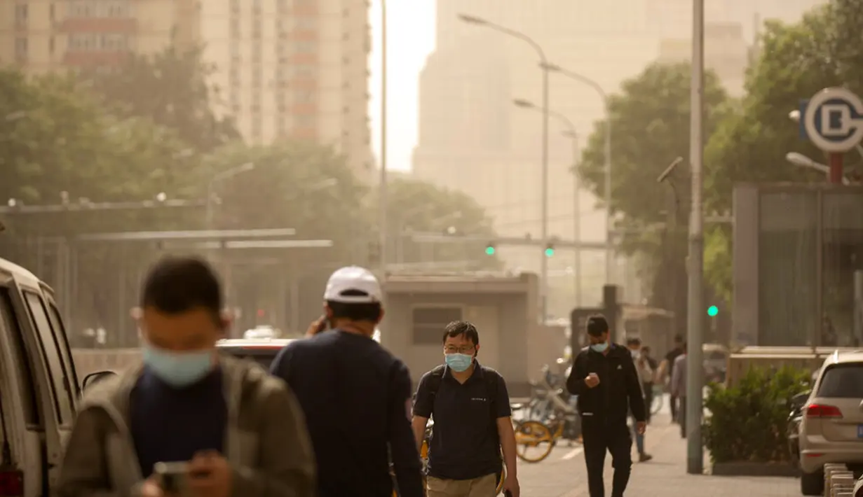 Orang-orang yang memakai masker wajah berjalan di sepanjang jalan saat badai pasir di ​Beijing, China, Kamis (6/5/2021). Debu dan badai pasir akhir musim semi mengirim indeks kualitas udara melonjak di Ibu Kota China pada hari ini. (AP Photo/Mark Schiefelbein