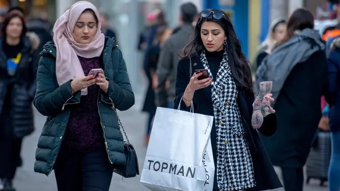 Pembeli memainkan ponsel sambil berjalan membawa kantong belanjaan di Oxford Street, London pada Sabtu (22/12). Menjelang natal, Oxford Street yang merupakan salah satu pusat perbelanjaan di jantung Kota London keramaiannya meningkat. (NIKLAS HALLE'N/AFP)