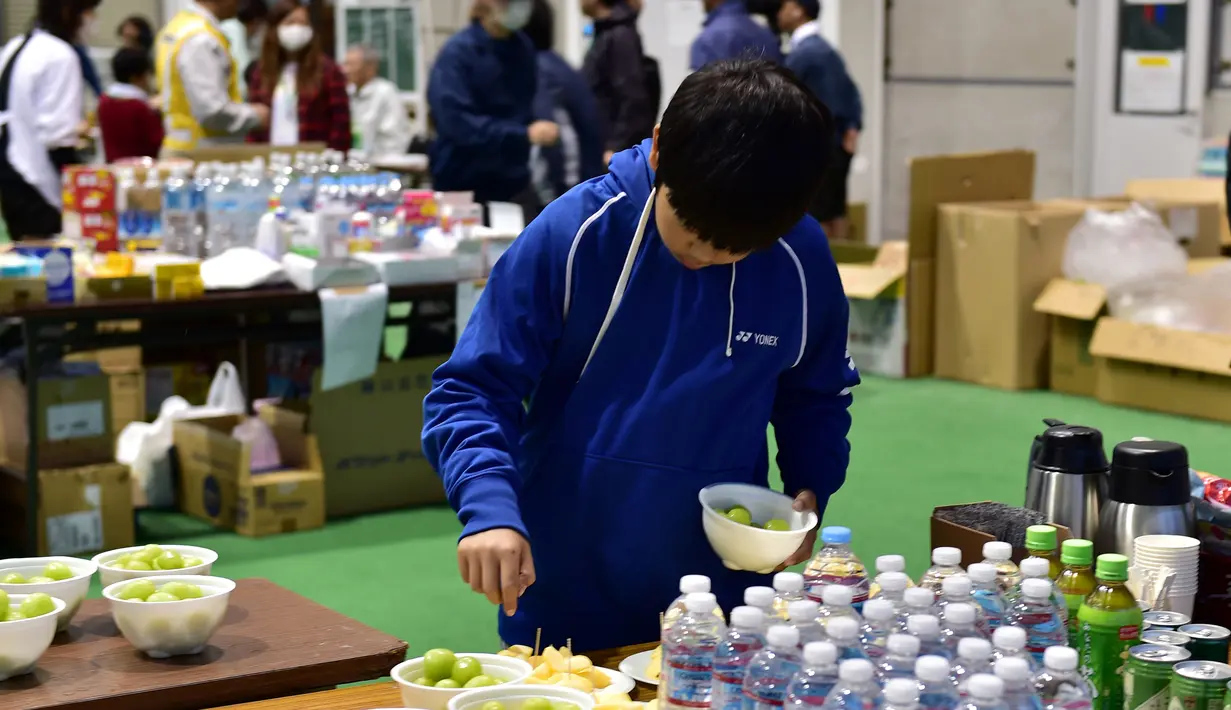 Seorang anak  mengambil buah di tempat penampungan evakuasi di Nagano, Jepang (14/10/2019). Puluhan ribu petugas tengah dikerahkan pada 14 Oktober untuk mencari warga yang hilang akibat terjangan Topan Hagibis tersebut. (AFP Photo/Kazuhiro Nogi)