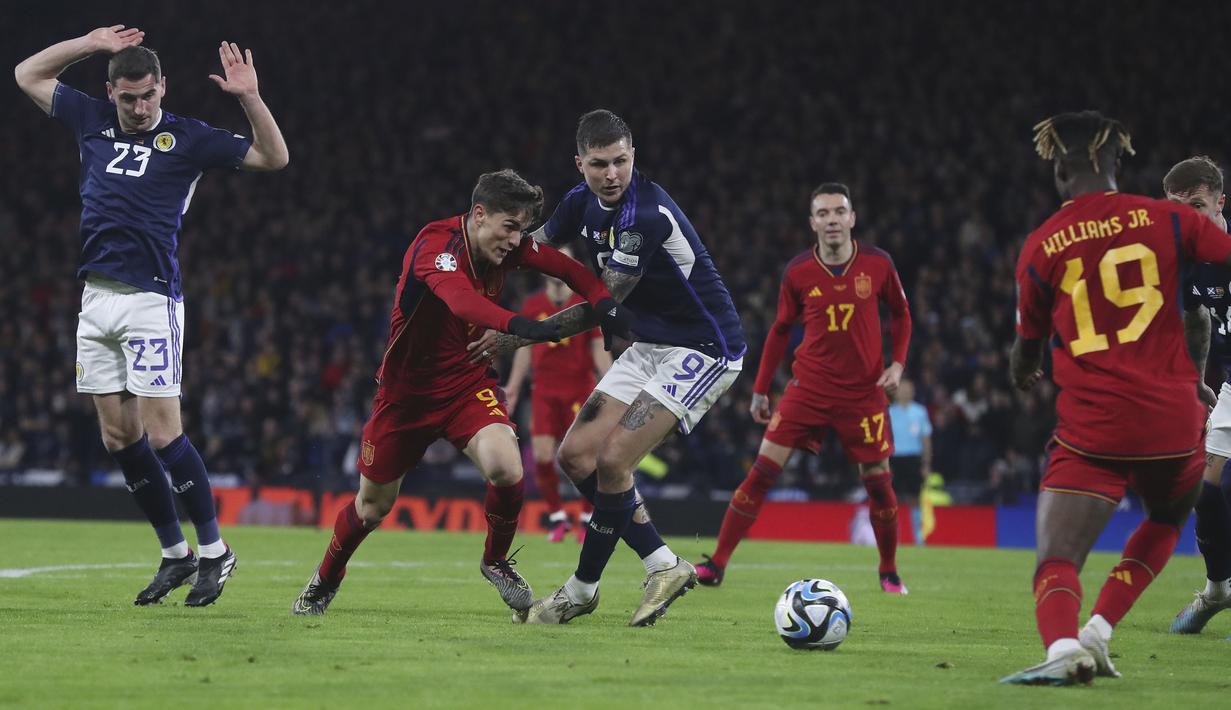 Pemain Spanyol, Gavi (tengah kanan) berebut bola dengan pemain Skotlandia, Lyndon Dykes pada matchday kedua Kualifikasi Euro 2024 di Hampden Park, Glasgow, Skotlandia, Rabu (29/03/2023) WIB. Skotlandia berhasil menang dengan skor 2-0. (AP Photo/Scott Heppell)