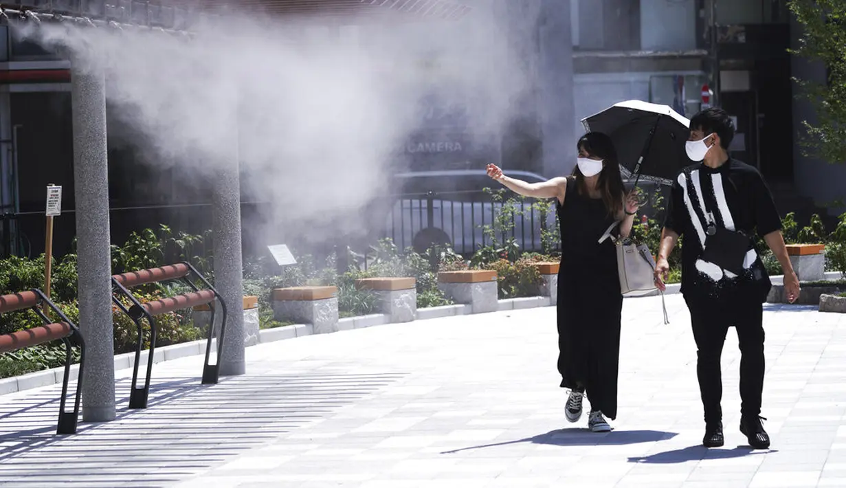 Seorang pria dan wanita mengenakan masker untuk mencegah penyebaran Covid-19 di bawah titik kabut dingin di Tokyo (12/8/2020). Menurut Badan Meteorologi Jepang, cuaca panas telah ditetapkan dengan suhu naik lebih dari 34 derajat Celcius (93,2 derajat Fahrenheit) di Tokyo. (AP Photo/Eugene Hoshiko)
