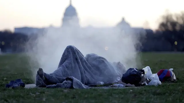 Gedung Capitol menjadi latar seorang gelandangan yang beristirahat di atas lubang uap di National Mall di kawasan Capitol Hill, Washington, DC, Amerika Serikat, pada 18 Desember 2019.