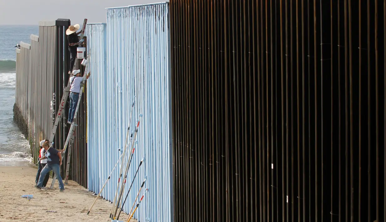 Sejumlah orang mengecat pagar perbatasan antara Meksiko dan Amerika Serikat di Playas Tijuana, Meksiko (10/12). Tembok dan pagar pembatas ini dibuat untuk mencegah masuknya imigran gelap Meksiko ke Amerika Serikat. (Reuters/Jorge Duenes)
