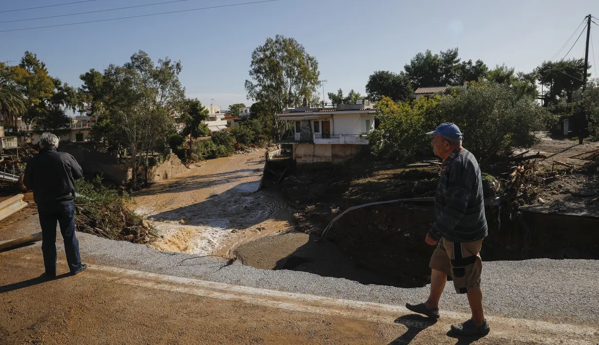 Warga memeriksa jalan yang rusak setelah badai di desa Kineta, Athena (25/11/2019). Pihak berwenang di Yunani mengatakan dua orang telah tewas. (AP Photo/Petros Giannakouris)