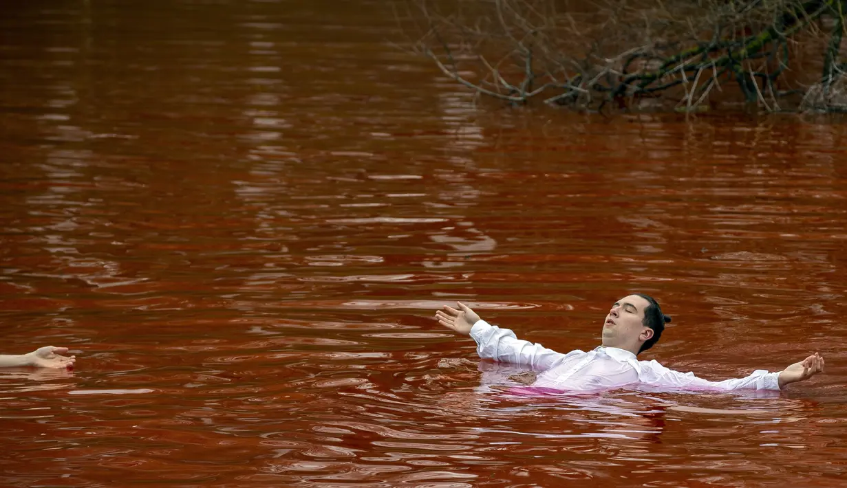 Orang-orang mandi dalam kolam warna merah untuk menandakan darah selama protes di depan kedubes Rusia di Vilnius, Lithuania, Kamis (7/4/2022). Pejabat Ukraina mengatakan 410 jasad warga sipil ditemukan di kota-kota wilayah Kiev yang baru-baru ini direbut kembali. (AP Photo/Mindaugas Kulbis)