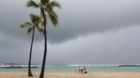 Para pengunjung pantai terlihat dengan latar belakang awan badai, di Pantai Waikiki, Honolulu (6/12/2021). Badai kuat yang membawa angin kencang dan hujan yang sangat deras membanjiri jalan-jalan dan meruntuhkan kabel listrik dan cabang-cabang pohon di seluruh Hawaii. (AP Photo/Marco Garcia)