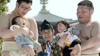 Pegulat sumo menggendong bayi dan membuat suara-suara serta wajah aneh agar bayi menangis.