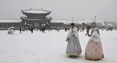 Pengunjung yang mengenakan pakaian tradisional hanbok berjalan di tengah salju di istana Gyeongbokgung di pusat kota Seoul, Korea Selatan, Sabtu (30/12/2023). (Jung Yeon-je / AFP)