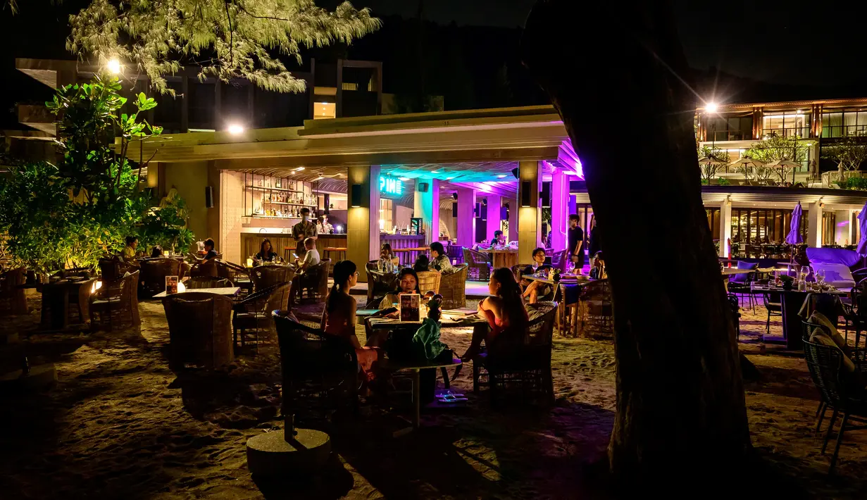 Orang-orang duduk di sebuah bar, saat para turis memanfaatkan program "Kotak Pasir Phuket" untuk pengunjung yang divaksinasi penuh terhadap virus corona Covid-19 di pulau Phuket Thailand (25/10/2021). (AFP/Mladen Antonov)