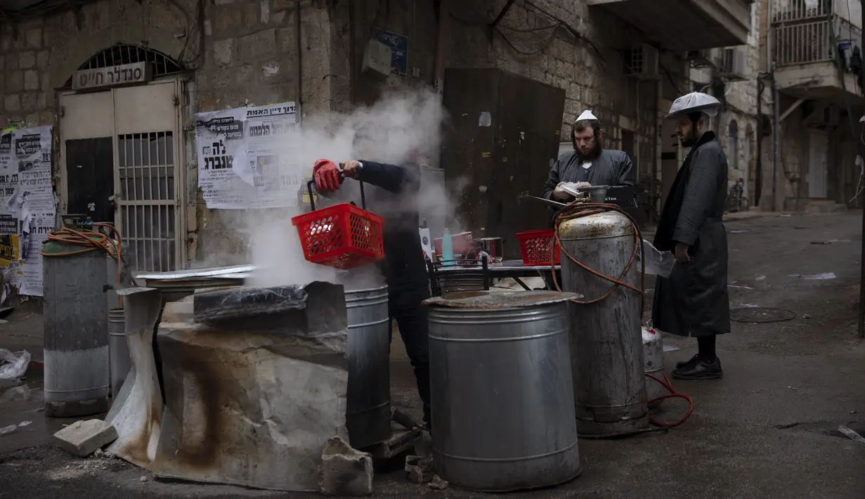 Seorang pria Yahudi ultra-Ortodoks mencelupkan peralatan masak ke dalam air mendidih untuk menghilangkan sisa-sisa ragi sebagai persiapan untuk hari raya Paskah Yahudi di Yerusalem (26/3/2021).  (AP Photo/Oded Balilty)