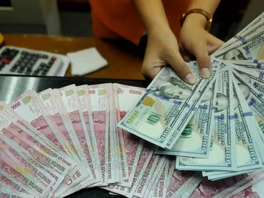 Petugas menunjukkan uang pecahan US$100 di penukaran uang, Jakarta, Rabu (12/8/2015). Reshuffle kabinet pemerintahan Jokowi-JK, nilai rupiah terahadap Dolar AS hingga siang ini menembus Rp 13.849. (Liputan6.com/Johan Tallo)