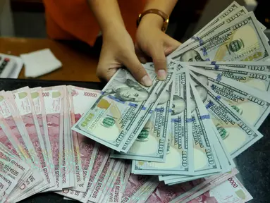 Petugas menunjukkan uang pecahan US$100 di penukaran uang, Jakarta, Rabu (12/8/2015). Reshuffle kabinet pemerintahan Jokowi-JK, nilai rupiah terahadap Dolar AS hingga siang ini menembus Rp 13.849. (Liputan6.com/Johan Tallo)