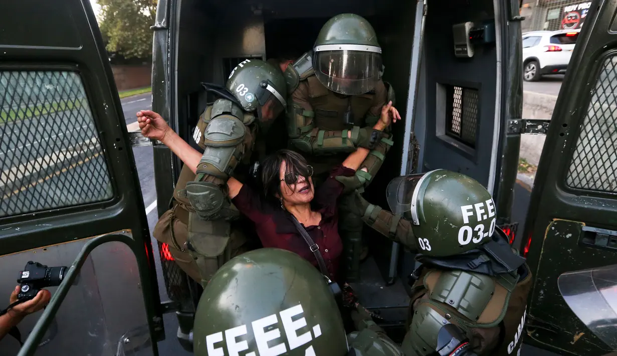 Seorang wanita dimasukan ke dalam mobil polisi anti huru hara saat melakukan demonstrasi di luar kedutaan AS di Santiago, Chili (14/4). (AP / Esteban Felix)