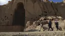 Orang-orang Hazara berjalan di situs patung Buddha raksasa yang dihancurkan oleh Taliban pada 2001 di Provinsi Bamiyan, Afghanistan, 3 Maret 2021. Terletak di jantung pegunungan Hindu Kush, di tebing indah lembah Bamiyan terdapat gua yang berisi kuil, biara, dan lukisan Buddha. (BANGUN KOHSAR/AFP)