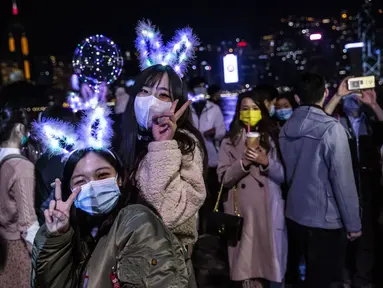 Dua wanita berpose di samping tepi perairan Pelabuhan Victoria di Hong Kong (1/1/2020). Meskipun ada pembatasan virus corona COVID-19 dan kembang api Tahun Baru dibatalkan, orang-orang berkumpul untuk merayakan Tahun Baru. (AFP/Isaac Lawrence)