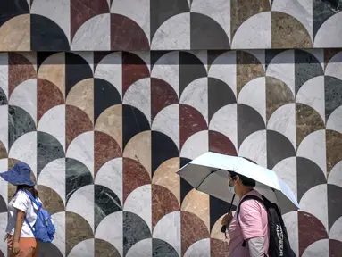 Orang-orang menggunakan topi matahari dan payung untuk melindungi diri dari sinar matahari saat mereka berjalan di luar pusat perbelanjaan pada hari yang panas di luar musimnya di Beijing, Sabtu, 24 Juni 2023. (AP Photo/Mark Schiefelbein)