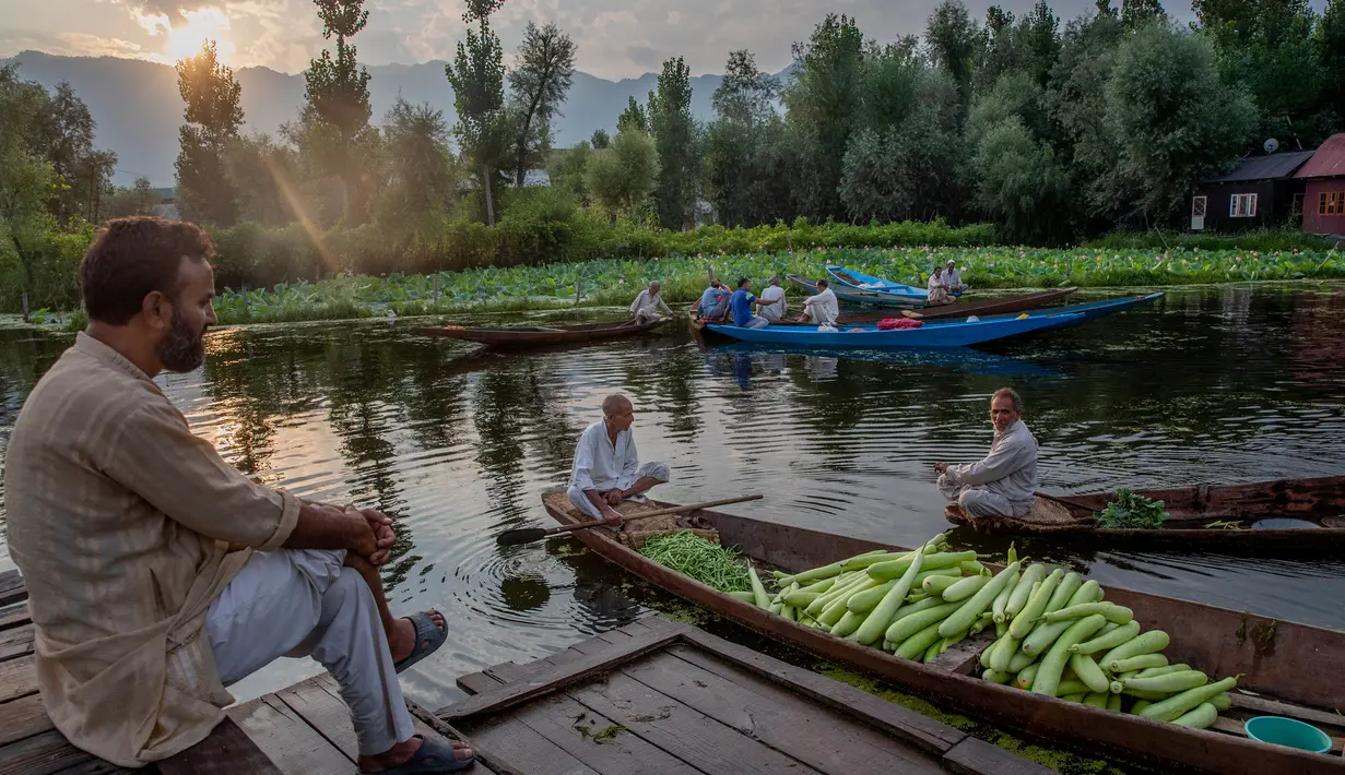 Seorang pria Kashmir menyaksikan orang lain menjual produk mereka di pasar sayur terapung di Danau Dal di Srinagar, Kashmir yang dikuasai India pada 26 Juli 2020. Sayuran yang diperdagangkan di pasar terapung ini disuplai ke Srinagar dan banyak kota di lembah Kashmir. (AP Photo/Dar Yasin)