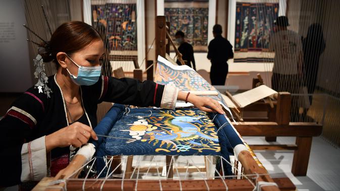 Seorang perempuan dari kelompok etnis Li memperagakan keahlian membuat bordir dengan pola naga dalam pameran selimut quilt di Museum Hainan, China pada 13 November 2020. Pameran yang berlangsung sebulan penuh tersebut menampilkan 41 selimut quilt dengan bordir naga Li yang indah. (Xinhua/Guo Cheng)