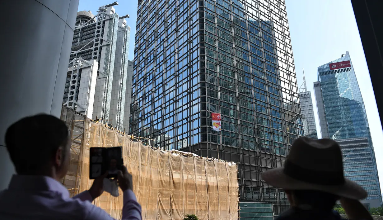 Warga menyaksikan Alain Robert yang dijuluki 'French Spiderman' memanjat gedung pencakar langit Cheung Kong Center di Hong Kong, Jumat (16/8/2019). Pria berusia 57 tahun tersebut memanjat Cheung Kong Center dalam kondisi panas dan lembab pada Jumat pagi. (Lillian SUWANRUMPHA/AFP)