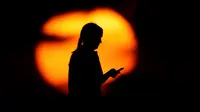 Seorang wanita melihat teleponnya di sebuah taman ketika matahari terbenam di Kansas City, Missouri, Amerika Serikat, Senin (29/6/2020). Matahari terbenam dan matahari terbit lebih cerah dari biasanya belakangan ini karena debu di atmosfer dari awan debu Sahara. (AP Photo/Charlie Riedel)