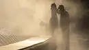 Seorang gadis kecil menyentuh kepala ayahnya saat mereka diselimuti kabut dari air mancur umum di Bukares, Rumania, Kamis (13/7/2023). (AP Photo/Andreea Alexandru)