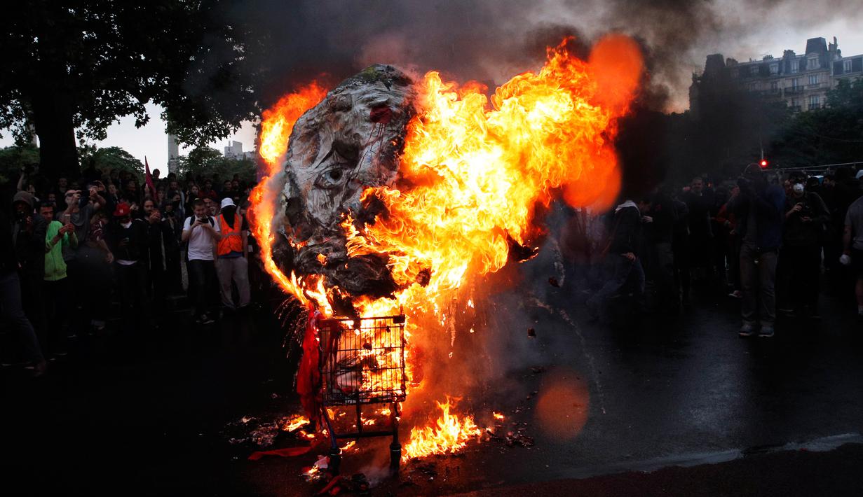 Sebuah topeng raksasa yang menggambarkan Presiden Prancis Emmanuel Macron dibakar selama terjadi demonstrasi di Paris, Prancis (23/5). (AP/Christophe Ena)