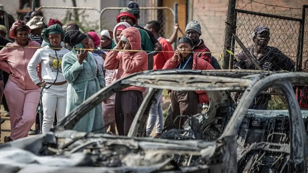 Warga berdiri di balik garis polisi di dekat lokasi penembakan di sebuah bar di Johannesburg, Afrika Selatan, Minggu (27/9/2026).