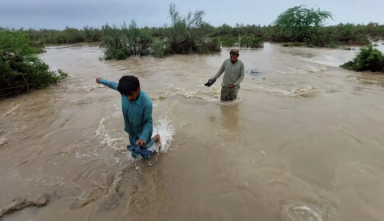 Penduduk desa melintasi daerah banjir untuk pindah ke tempat yang lebih tinggi setelah hujan lebat, di Lasbella, sebuah distrik di provinsi Baluchistan barat daya Pakistan (26/7/2022). Para pejabat mengatakan, pada hari Rabu, penyelamat yang didukung oleh pasukan menggunakan perahu dan helikopter untuk mengungsi ratusan orang terdampar dari barat daya Pakistan, di mana banjir yang dipicu oleh hujan telah menewaskan 104 orang sejak bulan lalu. (AP Photo/Hamdan Khan)