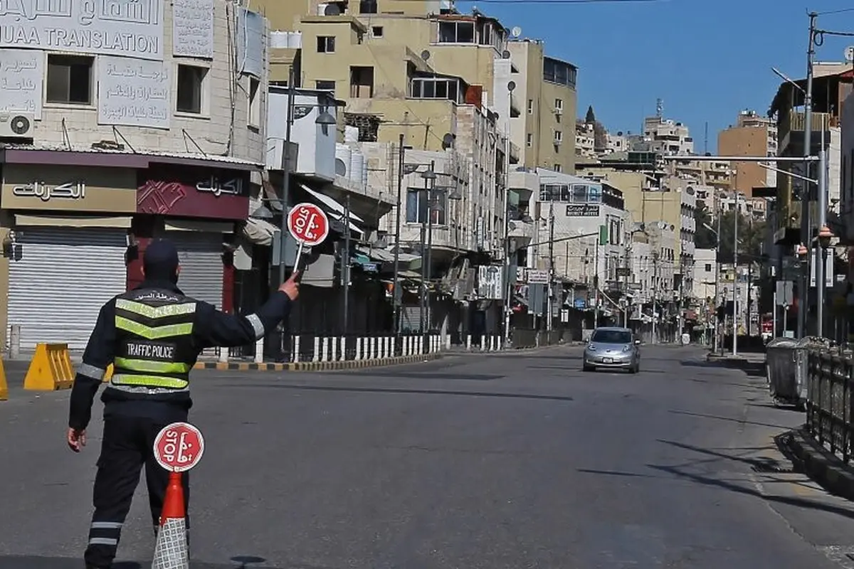 Seorang polisi memegang tanda berhenti di jalan yang hampir sepi di ibu kota Yordania, Amman, selama penguncian virus corona. [Khalil Mazraawi / AFP]