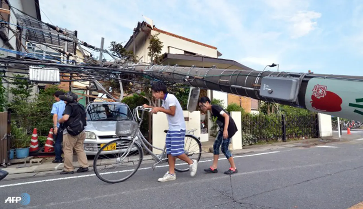 Warga melintasi tiang listrik yang tumbang akibat tornado.  Puluhan orang dilarikan ke rumah sakit, semuanya mengalami luka-luka ringan. (AFP/Yoshikazu Tsuno/wwn)