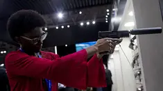 Seorang wanita memegang pistol dengan peredam di Pameran Internasional Pertahanan dan Keamanan LAAD di Rio de Janeiro, Brasil, Selasa, 11 April 2023. (AP Photo/Bruna Prado)