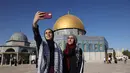 <p>Wanita Palestina berfoto selfie di depan masjid Dome of the Rock setelah shalat Idul Fitri pagi, yang menandai akhir bulan suci Ramadhan, di kompleks masjid Al-Aqsa di Yerusalem Tua (13/5/2021). (AFP/Ahmad Gharabli)</p>